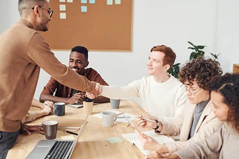 Team members in a meeting with a handshake between two people.